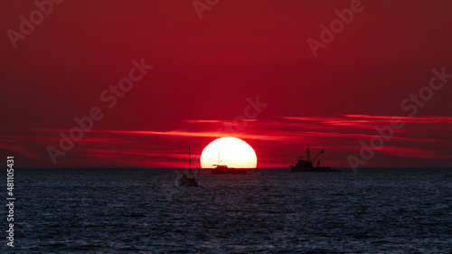 Big sunrise sunset over ocean sea horizon with silhouettes of boats. © astrosystem
