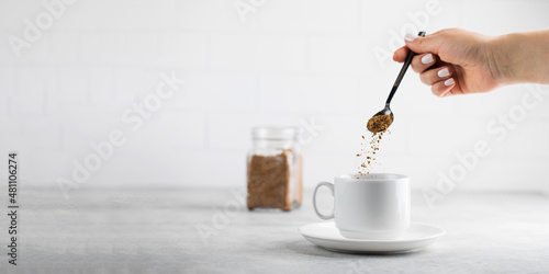 Quadro em tela A woman adds instant coffee to a white mug on grey stone table
