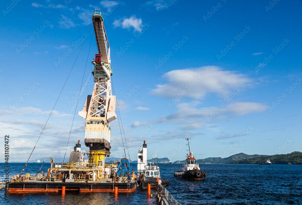 Fototapeta premium Shipment of a large floating crane by sea tugs on a semi-submersible transport vessel for its transportation by sea.