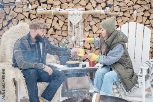 couple of young woman and man having fun, tenderness during teatime near fire in courtyard of suburban house in winter, concept of Christmas and New Year vacation on farm, family love and support