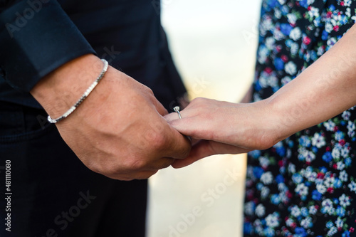 Man holding woman's hand, solitaire on woman's finger and close-up.