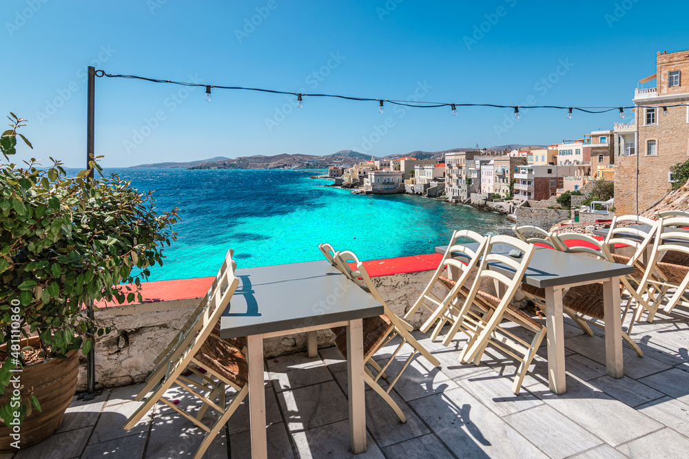 Fototapeta premium Empty chairs and tables of closed outdoor restaurant with sea view in Greece.