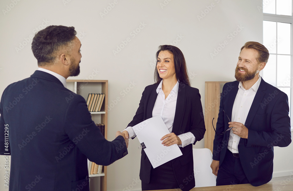 Clients exchanging handshake with lawyer. Happy young married couple smiling and shaking hands with financial advisor, thanking him for professional legal advice and help with their business documents Clients exchanging handshake with lawyer. Happy young married couple smiling and shaking hands with financial advisor, thanking him for professional legal advice and help with their business documents