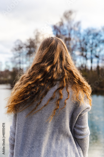 Rückansicht von einer jungen Frau mit langen lockigen Haaren an einem See. Natur, Schönheit.
