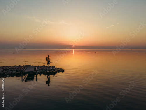 Sunrise. A man stands on the shore of a reservoir. Aerial view. © liukovmaksym