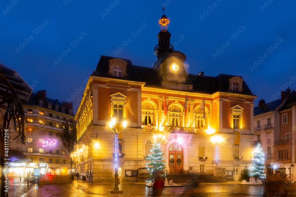 Night view of Chambery city hall surrounded by fir trees and street lamps decorated with traditional Christmas lights in central square in winter, France