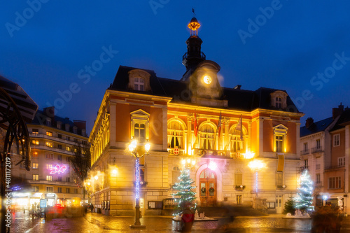 Night view of Chambery city hall surrounded by fir trees and street lamps decorated with traditional Christmas lights in central square in winter, France