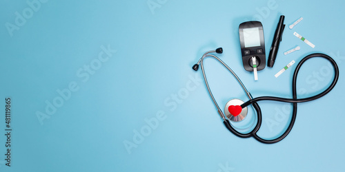 Diabetes equipment, glucose level blood test on blue background with copy space. Diabetic items to control diabetes blood sugar meter, lancet, test strip and lancing device with stethoscope