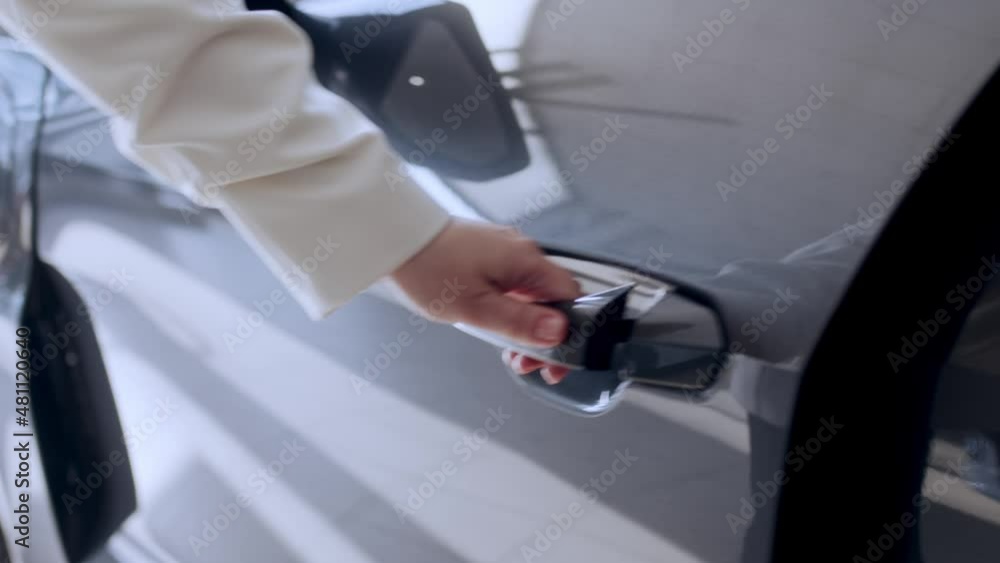 A woman, a driver, a customer opens the door of the driver's seat of an electric car, gets behind the wheel of a new luxury car and closes the door. Close-up. Car dealership, car business. Cinema 4k A woman, a driver, a customer opens the door of the driver's seat of an electric car, gets behind the wheel of a new luxury car and closes the door. Close-up. Car dealership, car business. Cinema 4k