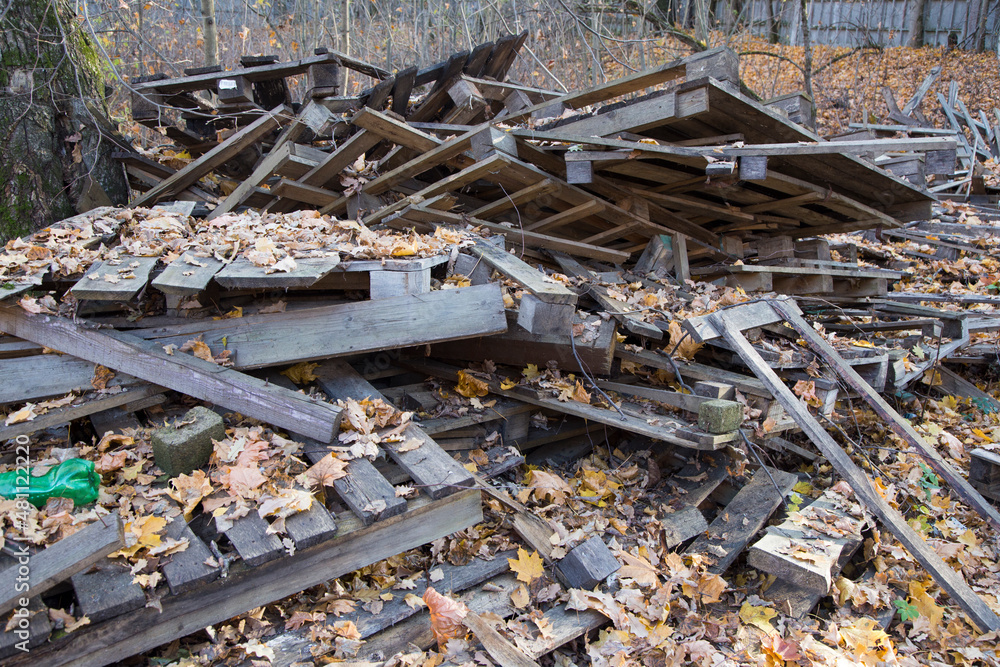 scattered pile of old dirty wooden pallets, wood planks and hardwood timber boards on autumn dry and yellow leaves ground scattered pile of old dirty wooden pallets, wood planks and hardwood timber boards on autumn dry and yellow leaves ground