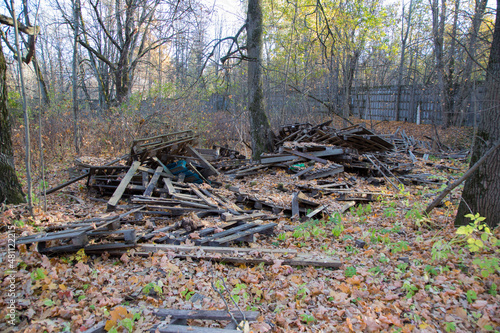 Fototapeta Naklejka Na Ścianę i Meble -  scattered pile of old dirty wooden pallets, wood planks and hardwood timber boards on autumn dry and yellow leaves ground