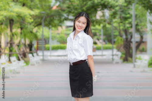 Young Asian woman student who has blond long hair smiles and looks at to camera while standing in university with outdoor garden tree background. © nut_foto