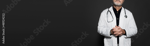 partial view of senior doctor with clasped hands isolated on black, banner.