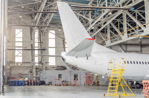 Passenger aircraft on maintenance of engine and fuselage repair in airport hangar, tail view.