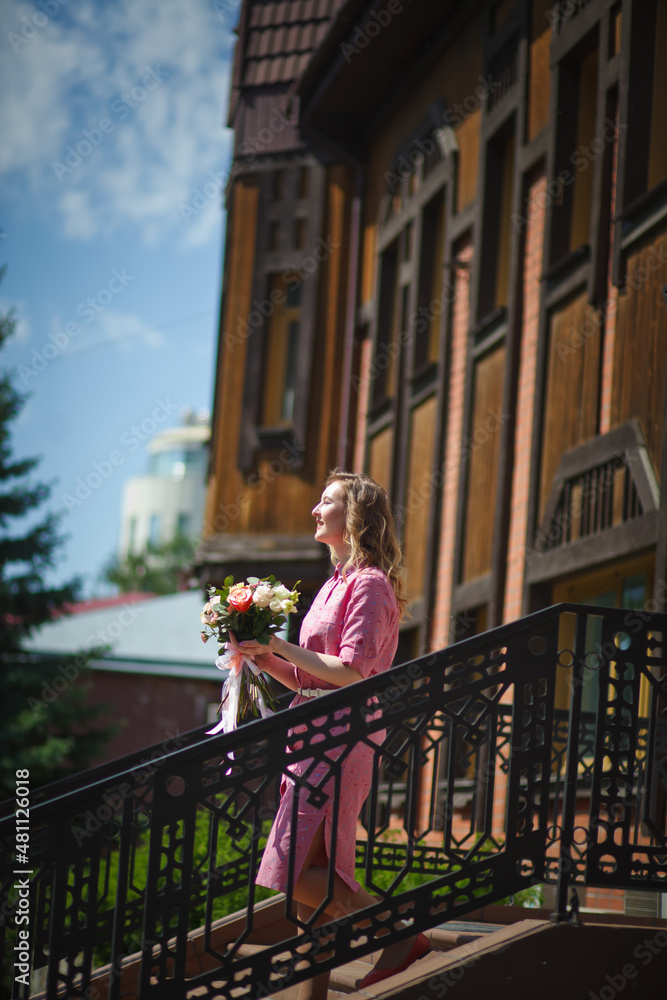 Young happy blonde woman in a pink dress with a large bouquet of flowers walks around the old European city and enjoys life on a summer day, beautiful portraits with a huge bouquet of flowers.