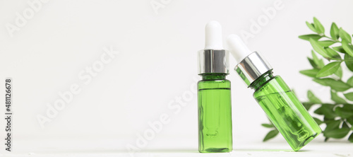 Green glass dropper bottles on white background with leaves. Cosmetic container mock-up. Background for branding and packaging presentation. Natural skincare beauty product concept