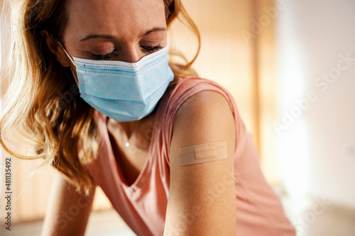 A woman with mask in hospital showing her shoulder after covid 19 vaccination. Vaccination, inoculation and health care.