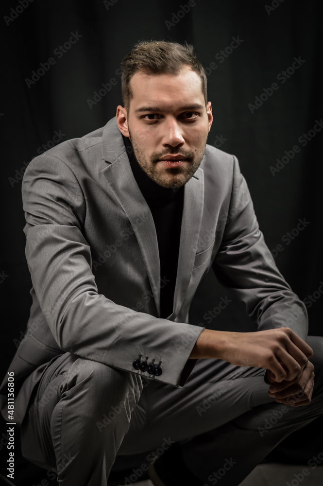 portrait of a young man in a gray suit and a black turtleneck, crouched on the ground looking intently