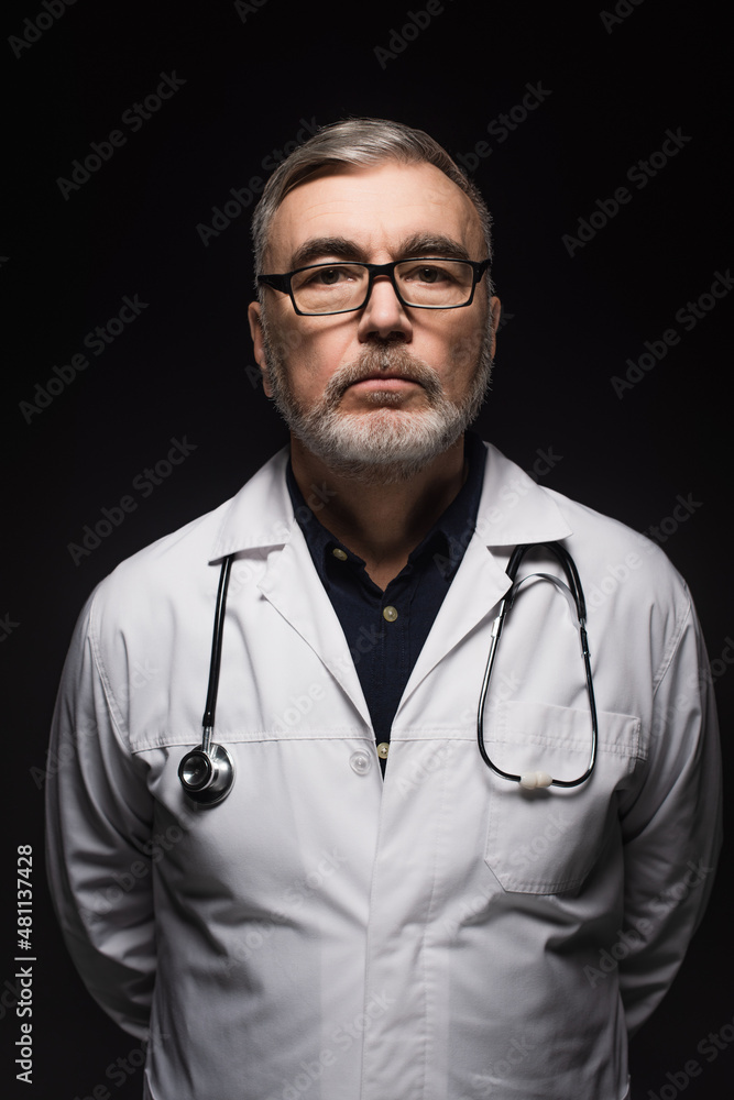 senior bearded doctor with stethoscope looking at camera isolated on black. senior bearded doctor with stethoscope looking at camera isolated on black.