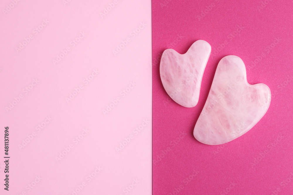 Fototapeta premium Rose quartz face massage stones on two color pink and crimson background with empty space for your design. 