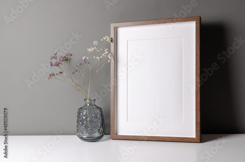 Fotografering Vertical wooden frame mockup for artwork, photo and print presentation on white table over grey wall, dry flowers in vase