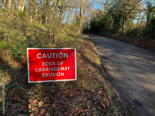 A roadside sign with white lettering on red background says 'Caution Edge of Carriageway Erosion'. photo