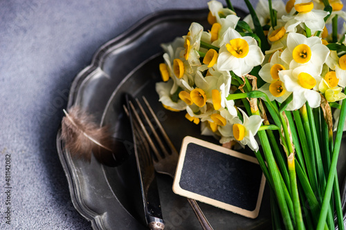Overhead view of a bunch of narcissus flowers on a pewter plate with cutlery and a chalk nameboard photo