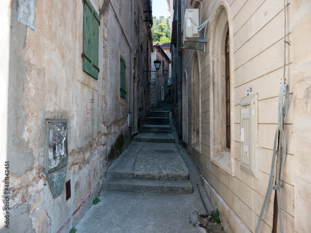 Narrow path in old house walls with stone stairs, windows and iron lamp