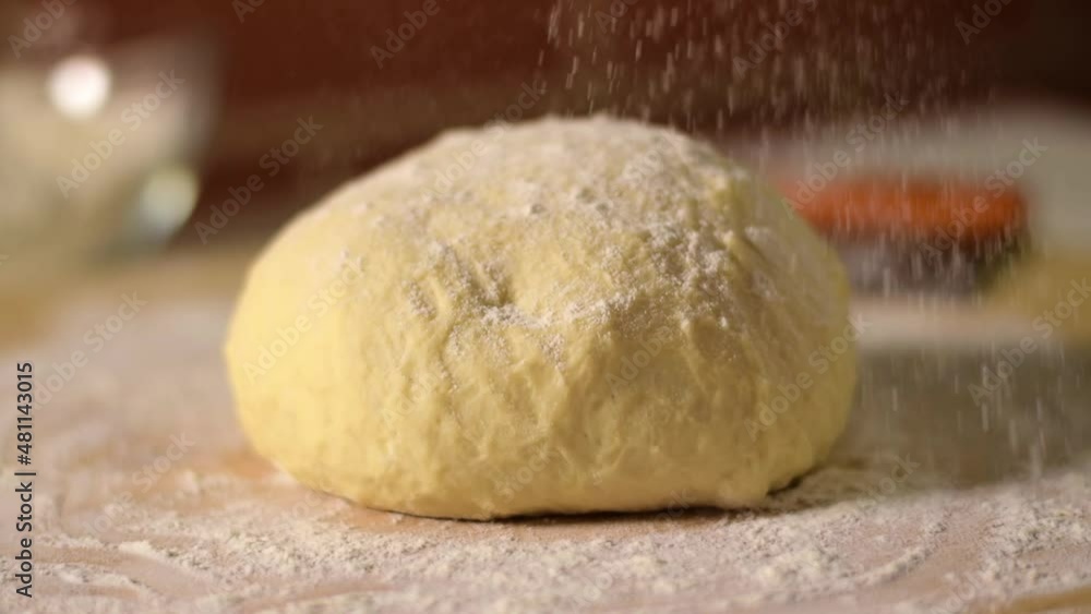Baker is sprinkling yeast dough ball with flour on the board before rolling. Baking at home Baker is sprinkling yeast dough ball with flour on the board before rolling. Baking at home