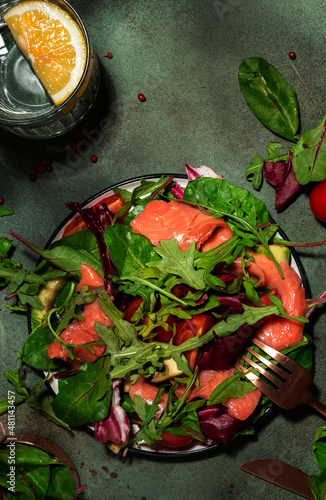 Fresh salmon salad with beet leaves, radicchio, tomatoes, lemon and olive oil dressing for keto and low carb diet. Rusty green background, hard light, top view, copy space
