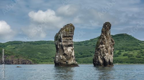 Amazing cliffs with steep slopes, devoid of vegetation, rise in the Pacific Ocean. Birds' nests on bare rocks. Picturesque green hills of the Kamchatka coast against the blue sky. Avacha Bay. 