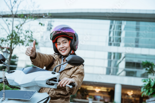 Woman wearing helmet while riding motorbike with thumbs up