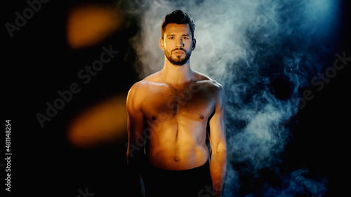 muscular sportsman looking at camera with smoke on black