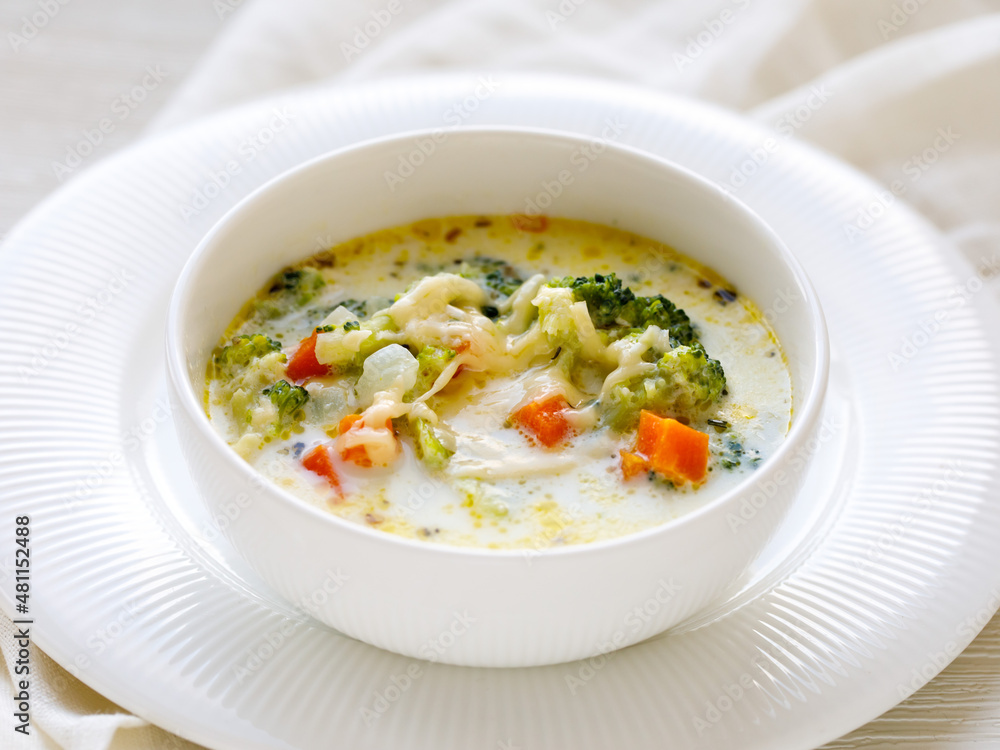 Healthy lunch colorful broccoli cheese soup in a bowl close-up on white table. Horizontal, top view from above, selective focus