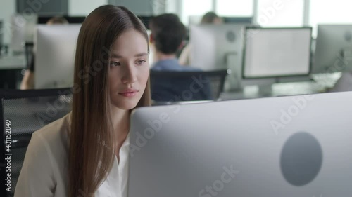 Portrait of Young Woman in Open Space Office Working on Decktop Computer. Female Professional Typing on PC Keyboard at Office Workplace. Portrait of Positive Business Girl Looking at Computer Screen photo