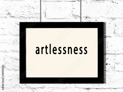Black frame hanging on white brick wall with inscription artlessness