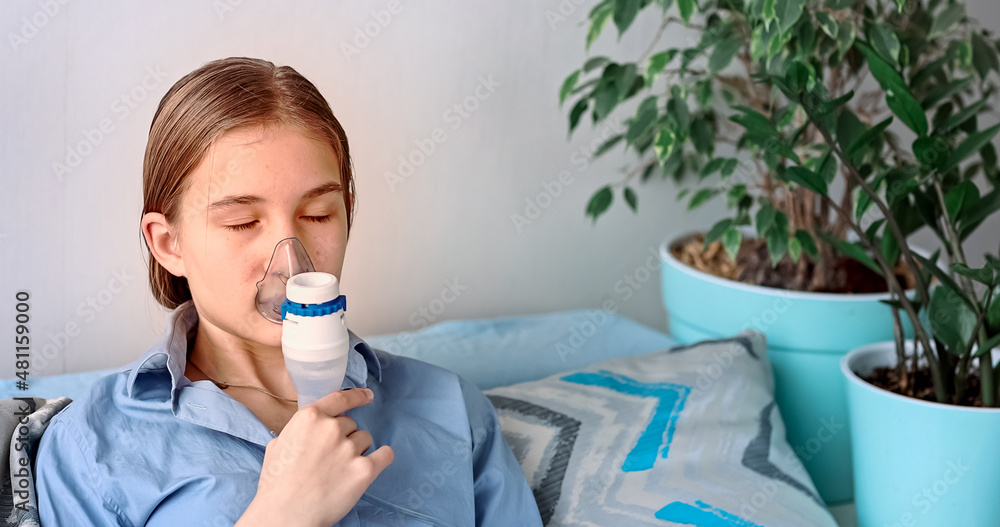 Teenage girl makes inhalation with a nebulizer equipment. Sick child holding inhalator in hand and breathes through an inhaler at home