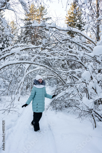pretty stylish girl walks in winter forest among trees covered with snow. Girl is wearing warm jacket, white hat and scarf. Comfortable clothes for walking in winter. Vertical photo