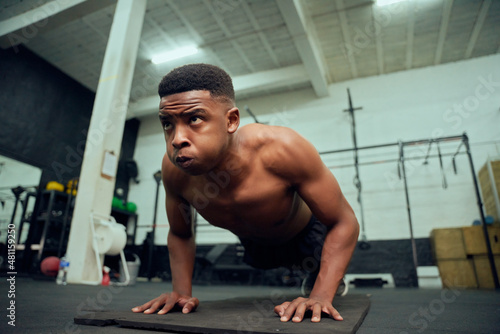 Young African American male doing push-ups in the gym. Mixed race, male personal trainer doing cross fit indoors. High quality photo