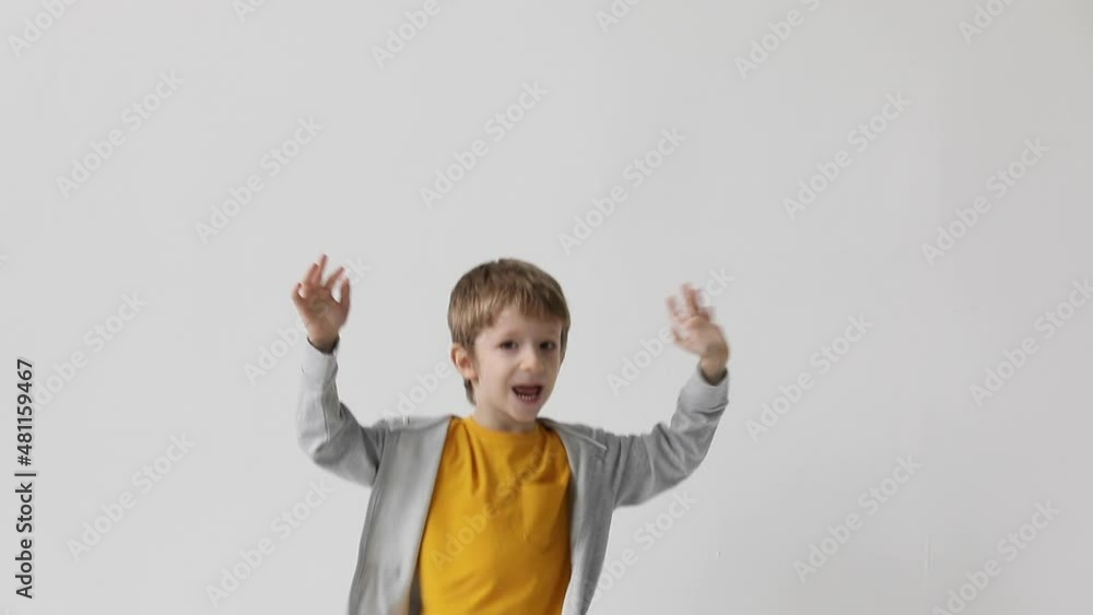 Cute little boy having fun close-up joyfully jumping waving his arms, celebrating victory, over white wall background. Cute little boy having fun close-up joyfully jumping waving his arms, celebrating victory, over white wall background.
