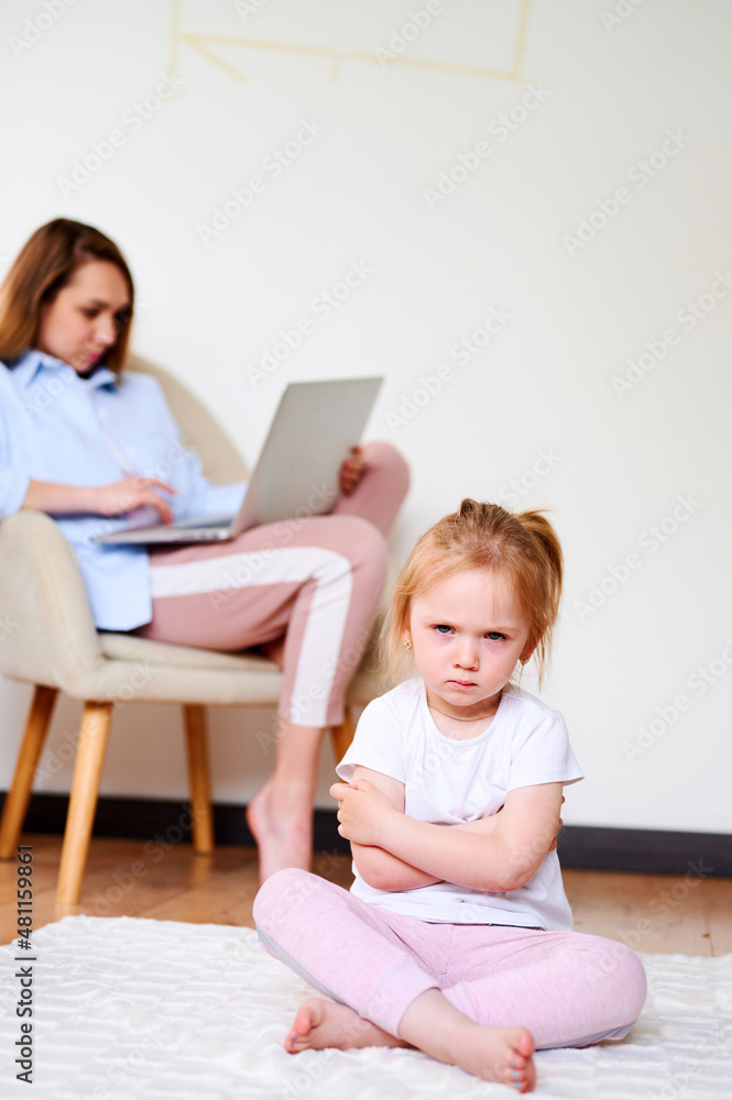 Upset little girl sitting lonesome while mother using laptop. Mother don't have time for daughter Upset little girl sitting lonesome while mother using laptop. Mother don't have time for daughter