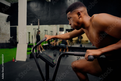 African American male using an elliptical trainer during cross training. Male athlete exercising intensely in the gym. High quality photo