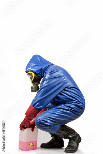 Man in blue rubber blue rubber protective suit, with gas mask, red rubber gloves and black rubber boots opens a canister with a red and corrosive cleaning liquid.