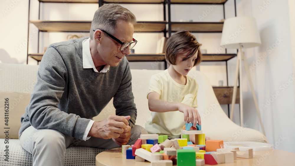 middle aged grandfather in glasses playing building blocks with boy middle aged grandfather in glasses playing building blocks with boy