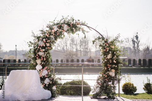 Festive arch decorated with composition of flowers and greenery in the backyard banquet area. Wedding ceremony with decor.