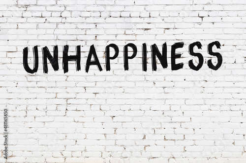 Φωτογραφία White wall with black paint inscription unhappiness on it