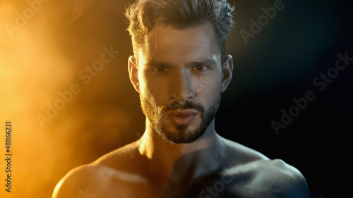 Portrait of muscular sportsman looking at camera near smoke on black with yellow lighting