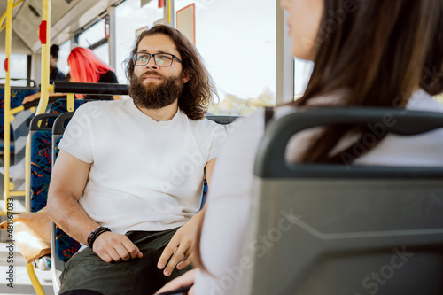 Man with long hair and thick beard wearing glasses takes public transport bus to work to meeting with friends looks out window observes bus stops afternoon in large agglomeration traffic jam rush hour photo