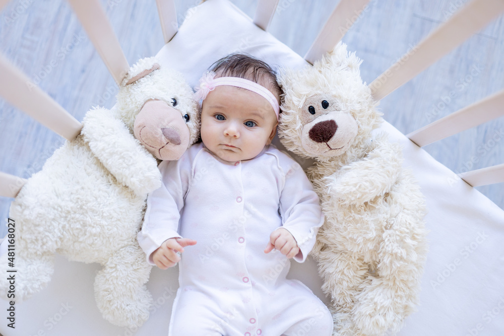baby girl with teddy bears smiling on the bed on a white cotton bed, falling asleep or waking up in the morning, cute newborn little baby at home in the crib close-up