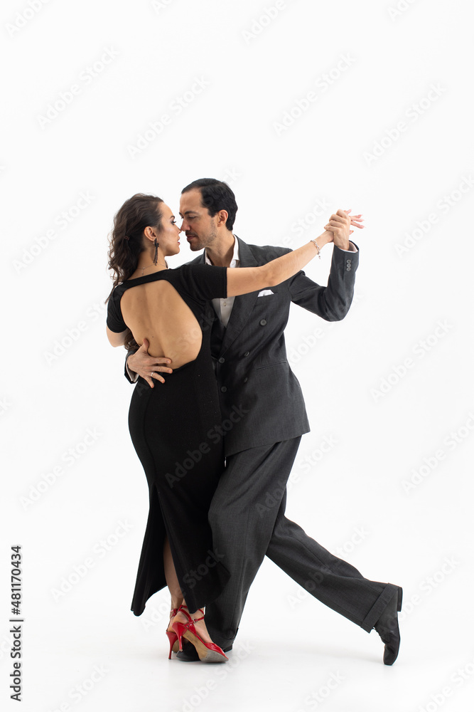 Couple of professional tango dancers in elegant suit and black dress with an open back pose in a dancing movement on white background. Handsome man and woman dance looking eye to eye. Couple of professional tango dancers in elegant suit and black dress with an open back pose in a dancing movement on white background. Handsome man and woman dance looking eye to eye.